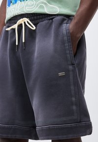 Close-up van donkergrijze casual shorts met witte aantrekkoord, zijzakken en klein zwart Nike-logo op het rechterbeen.