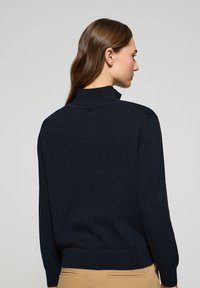 Pull-over en laine marine foncé avec un col haut, des poignets et un ourlet côtelés. Texture lisse, design ajusté et détails de couture aux épaules.