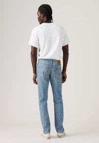 Φωτεινά μπλε τζιν με σχεδιασμό ίσιας γραμμής, με πίσω τσέπες, διακριτικές ραφές και καφέ δερμάτινο έμπλαστρο στη μέση.