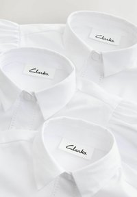 Kolm valget särki klassikaliste kraede ja nööpide kinnitustega, millel on "Clarks" silt. Tekstuuriga kangas ja peened detailid placket'il.
