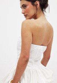 Vestido blanco sin mangas con un corsé ajustado y una falda volumétrica y fruncida. Tejido suave y un diseño limpio sin patrones o adornos visibles.