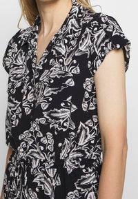 Robe noire avec motifs floraux blancs, manches courtes, col boutonné et taille à cordon de serrage pour un ajustement personnalisé.