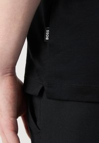 T-shirt nero realizzato in morbido tessuto, con uno spacco laterale e una piccola etichetta con "BOSS". Il materiale sembra liscio, aderente e casual.