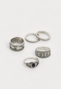 Ensemble de cinq anneaux en argent présentant divers motifs, y compris un motif d'éléphant, des motifs géométriques et un détail central en pierre noire.