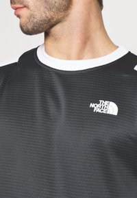 Maglietta nera a maniche corte in tessuto testurizzato, con colletto girocollo bianco e il logo bianco di "The North Face" sul petto.