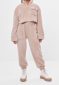 Zestaw dresowy z polaru w jasnobeżowym kolorze, zawierający krótki zapinany na zamek kurtkę z kieszenią oraz luźne spodnie z elastycznym pasem.