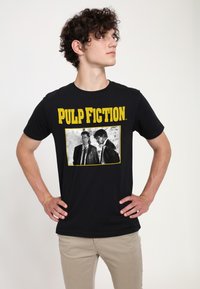 Černé tričko s �žlutým nápisem "PULP FICTION" a černobílým obrázkem dvou mužů ve smokingu. Měkká bavlněná tkanina s volným střihem.