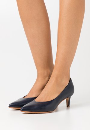 Escarpins en cuir bleu marine avec un bout pointu, un design à découpes subtile, et un petit talon stiletto. Texture lisse et style minimaliste.