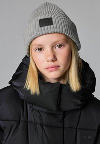 Harmaa ribbipipo mustalla tarralla, yhdistettynä mustaan toppatakkiin, jossa on korkea kaulus ja tikkikuvio. Yksinkertainen tausta.