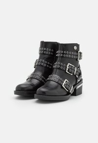 Bottes noires en cuir à la cheville avec plusieurs sangles ornées de clous en argent et de boucles. Talon carré et design à bout rond ; finition élégante et polie.