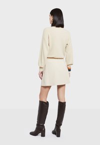 Suéter beige claro, falda mini crema y botas negras hasta la rodilla con tacones gruesos. Textura suave y corte relajado con mangas abullonadas.