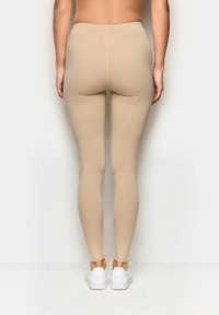 Leggings beige in un design aderente con una texture liscia, dotati di una vita alta e taglio alla caviglia, abbinati a sneakers bianche.