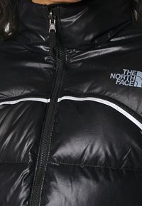 Black puffer jacket with high collar, featuring a zip closure, reflective white accents, and a logo on the left chest area.