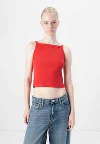 Punainen ribbed crop-top, jossa kapeat hihnat ja neliskanttinen kaula-aukko, yhdistetty korkeavyötäröisiin vaaleansinisiin farkkuihin, jotka tarjoavat rentoa istuvuutta.