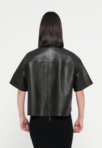 Svart lær cropped topp med korte ermer, med en jevn tekstur og enkle, rene linjer. Designet med detalj i sømmen bak.
