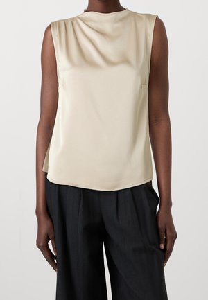 Beżowy top bez rękawów wykonany z gładkiej tkaniny, z okrągłym dekoltem i delikatnym drapowaniem, w zestawieniu z luźnymi czarnymi spodniami.
