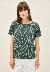 T-shirt verde a maniche corte con un motivo foglioso in verde chiaro. Presenta un collo rotondo e una vestibilità rilassata. Il tessuto appare morbido e liscio.