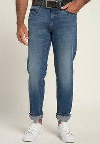 Vaqueros de mezclilla azul con un ajuste relajado, que cuentan con un diseño clásico de cinco bolsillos, puños doblados y un cinturón negro. Combinados con deportivas blancas.