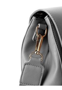 Detail šedé kožené kabelky s zlatým kovovým klipem a uchycením řemínku, s prošívanými akcenty a hladkým texturovaným povrchem.
