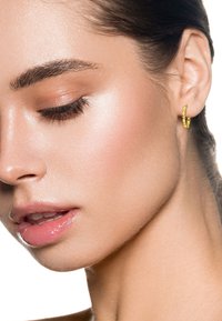 Ritratto ravvicinato di una donna dalla pelle liscia che indossa un piccolo orecchino a cerchio d'oro con gemme trasparenti, occhi chiusi e labbra leggermente socchiuse.