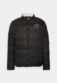 Svart vadderad jacka med horisontellt quiltat mönster, hög krage, framdragkedja och vit logotypdetalj på vänster bröst.