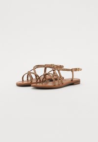 Sandales en cuir marron avec des brides tressées, semelle plate, bride de cheville avec boucle en métal et semelle perforée pour le confort.