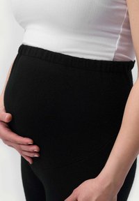 Svarta gravidleggings med ett mjukt, stretchigt tyg, som har ett högt midjeband och en slät yta som omfamnar en rundad mage.