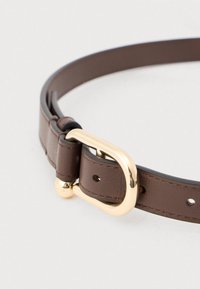Brunt læderbælte med spænde i guldmetal og en rund detalje. Har fem huller til justering og en glat tekstur.