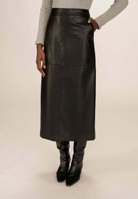 Robe mi-longue en cuir noir avec une texture lisse, dotée d'une taille haute et de poches latérales, associée à des bottes ajustées noires haute jusqu'aux genoux.