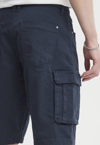 Sötét tengerészkék rakodó rövidnadrág tartós pamutból, oldalzsebekkel, varrott díszítésekkel és klasszikus szabással.