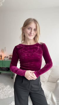 Burgundska baršunasta majica dugih rukava s teksturiranim detaljima, okruglim izrezom i uskim fitom, u kombinaciji s crnim hlačama visokog struka.