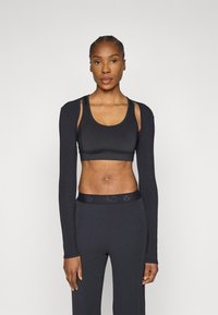 Μαύρο crop top με μακριά μανίκια και ανοίγματα στους ώμους, συνδυασμένο με μαύρο ψηλόμεσο κολάν με υφασμένη ζώνη στη μέση.