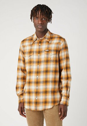 Camicia a quadri nei toni dell'arancione, crema e nero. Realizzata in tessuto morbido, con chiusura a bottoni, colletto a punta e due tasche sul petto.