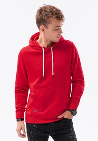 Červená mikina s kapucí, vybavená stahovací šňůrkou, přední kapsou a ribbed manžetami. Materiál je měkký a design má moderní, přiléhavý siluetu.