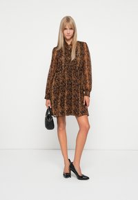 Leopardmønstret kjole i brune og sorte nuancer, med krave, lange puffærmer og et bølgende design. Parret med sorte højhælede sko og en lille taske.