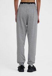 Graue Jogginghose mit elastischem Bund und schmalen Knöcheln. Merkmale einen schwarzen Logo-Bund. Kombiniert mit schwarzen Sportschuhen.
