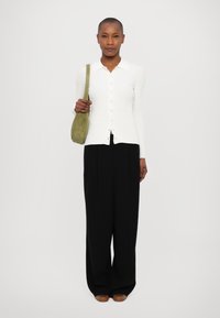 Witte lange mouwen button-up top, geribbelde textuur, gecombineerd met hoge taille zwarte broek en een kleine groene schoudertas.
