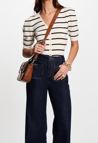 Stribet, kortærmet striktop i creme og sort med v-hals og knapper. Sammen med høj talje, mørk denim brede bukser og en brun crossbody taske.