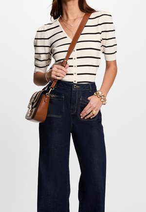 Gestreepte, kortemouwen gebreide top in crème en zwart, met een v-hals en knopen. Gecombineerd met hoge, donkere denim wijde broek en een bruine schoudertas.