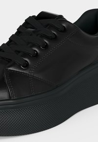 Sneaker platform in pelle nera con suola spessa e testurizzata e lacci neri, mostrando cuciture dettagliate e materiale superiore liscio.