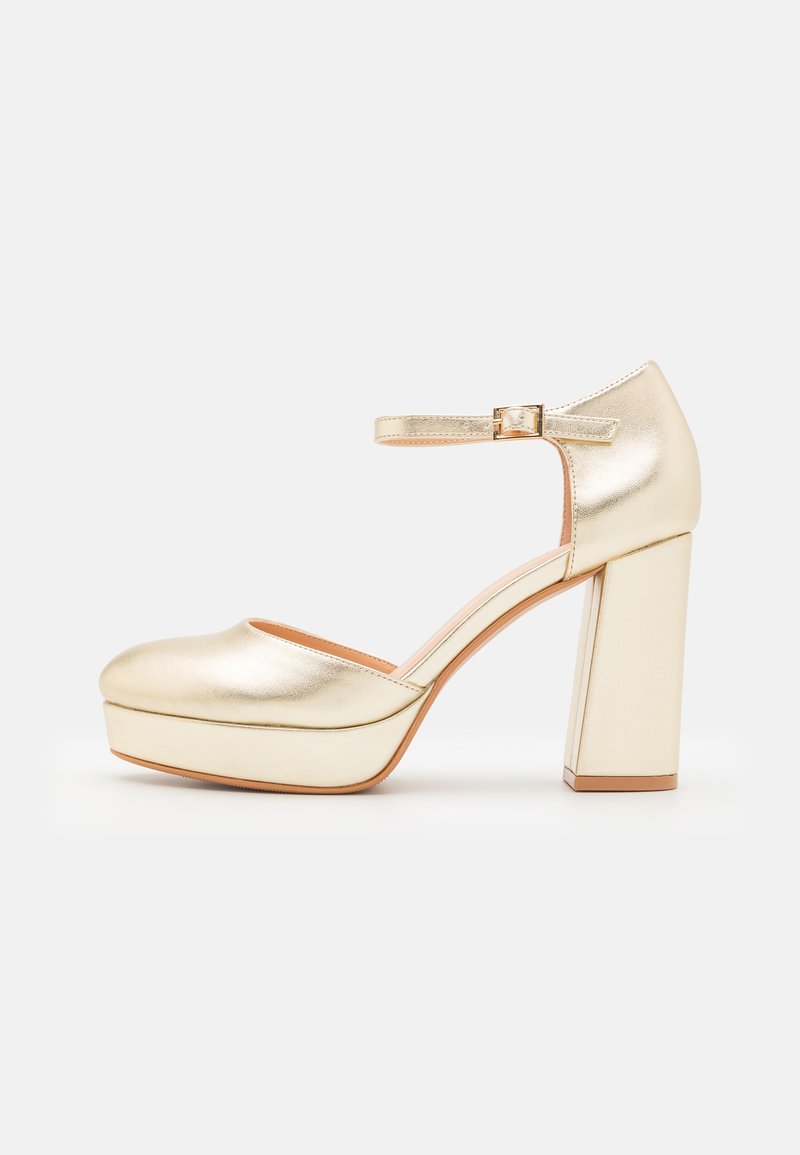 Chaussure à talon haut à plateforme dorée avec bout arrondi et bride à la cheville sur fond blanc.