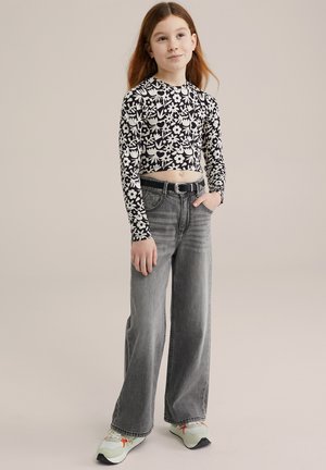 Top corto de flores en blanco y negro con mangas largas, combinado con unos pantalones vaqueros grises de tiro alto y corte holgado, y zapatillas verdes claras.