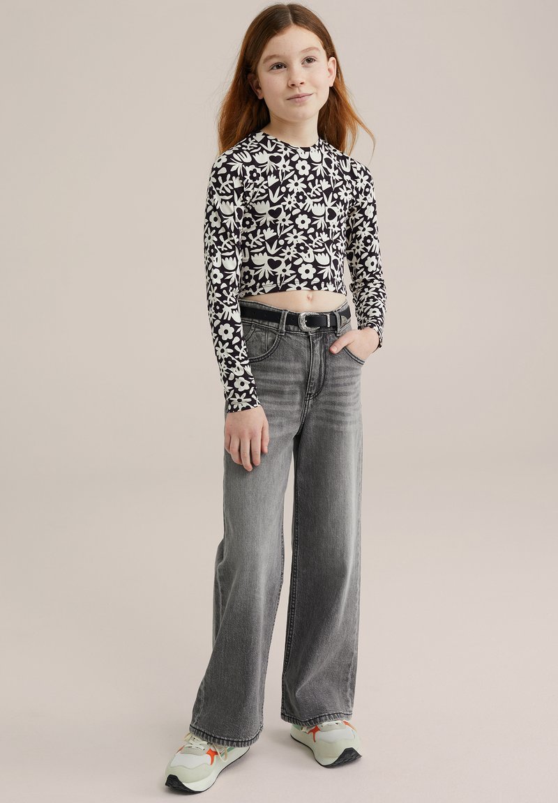 Fekete-fehér virágmintás, hosszú ujjú crop top, amelyet magas derekú, bőszárú szürke farmernadrággal és világos zöld tornacipővel párosítottak.