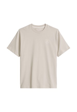 Béžové tričko s krátkými rukávy a kulatým výstřihem s malým tónovaným kruhovým logem na levé hrudi, zobrazené na bílém pozadí.