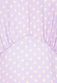 Tecido lavanda com pequenos pontos amarelos pálidos. Apresenta costura franzida na costura, criando textura e interesse visual.