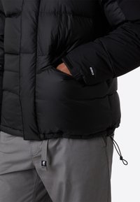 Sort pufferjakke med quiltet design, der har lynlåslommer på siderne og justerbar kant. Tekstureret materiale med elastiske manchetter.