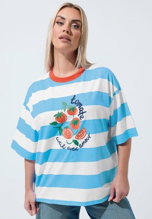 Kobieta ubrana w niebiesko-białą, szeroką koszulkę w paski z czerwonym kołnierzykiem i grafiką pomidora z francuskim tekstem z przodu.