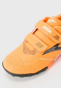 Oransje sportsko med svarte detaljer, teksturert syntetisk overdel og to justerbare borrelåsstropper. Har såle i sort gummimateriale med spor.