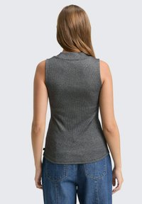 Ärmelloses graues Top mit feiner Textur, taillierter Passform und subtilen Kragen, kombiniert mit hochgeschnittenen blauen Jeans aus Denim mit Gesäßtaschen.