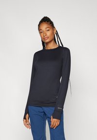 Long-sleeve black top made of smooth, stretchy fabric with thumbholes. Features a round neckline and subtle branding on the sleeve.